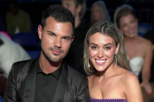 A couple posing and smiling at an event, with other attendees blurred in the background.