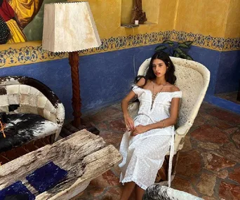 Woman in a white dress sitting on a cozy chair in a colorful room with rustic decor and cowhide furnishings.