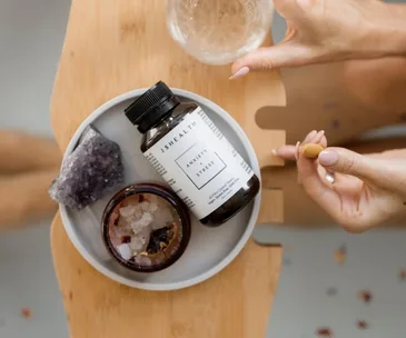 JSHealth Anxiety Stress bottle on a tray with a hand holding a capsule, beside a crystal and a jar of salts.