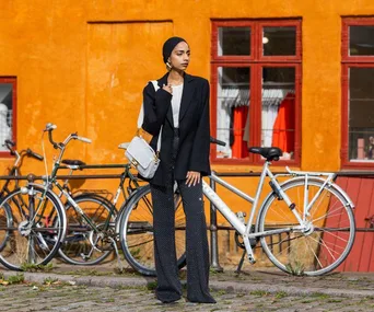 Fashionable woman in black blazer and dotted pants stands by a bike against an orange wall at Copenhagen Fashion Week.