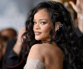 Rihanna with long, wavy hair, adorned in a sparkling outfit, turns her head slightly with a confident expression.