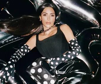 Person in black outfit with polka dot gloves, holding matching bag, surrounded by metallic balloons.