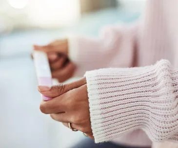 Person in a pink sweater holds a home pregnancy test, focusing on their hands.