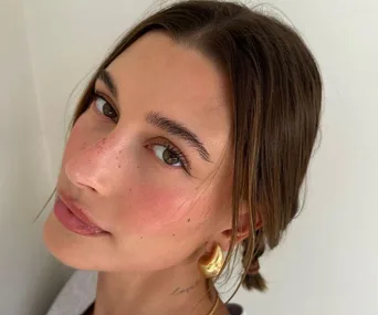 Close-up of a person with strawberry-inspired makeup, showing natural freckles, rosy cheeks, and glossy lips.