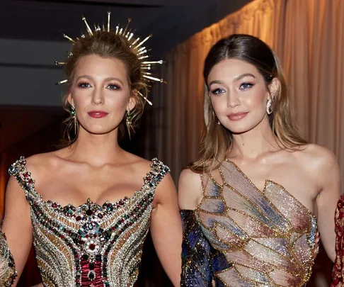 Two women in glamorous, shimmering gowns at a formal event, with one wearing a spiked headpiece.