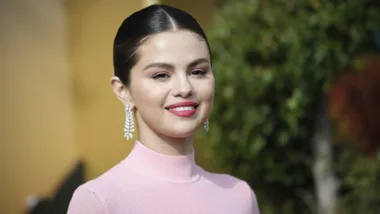 Smiling woman wearing pink top and earrings, with a blurred green background.