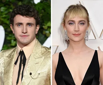 Two actors side by side, one in a beige suit with a bolo tie, the other in a black dress with sparkling earrings.