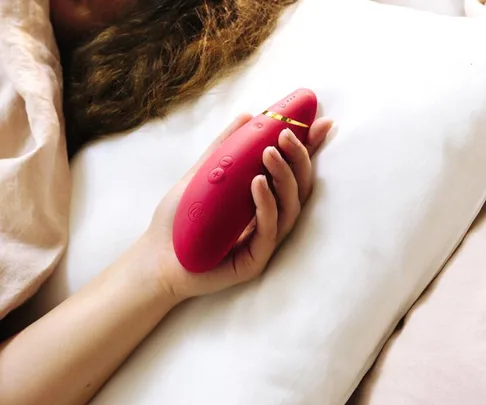 Person holding a red handheld electronic device with buttons, lying in bed.