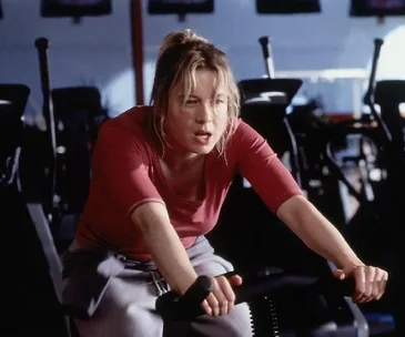 Person in a red top working out on an exercise bike in a gym setting.