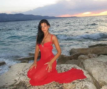 Woman in red dress sitting on rocks by the ocean at sunset.