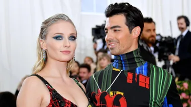 A couple dressed in colorful outfits at a formal event, standing together and smiling in front of a blurred crowd.