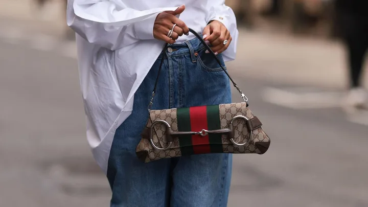 Person holding a Gucci Horsebit chain bag with GG logo and red-green stripe, wearing denim jeans and white shirt.