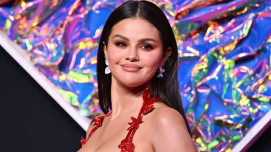 Selena Gomez at the MTV VMAs 2023 in a red dress with colorful background.