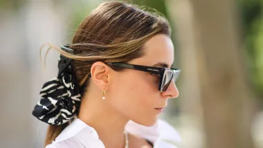 A woman with sunglasses and earrings, wearing a black and white hair scarf, side profile shot.