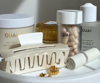 OUAI hair and body products displayed with a claw clip and gold earrings on a white surface.