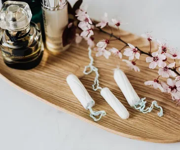 Tampons and cherry blossoms on wooden tray with perfume bottles in the background.