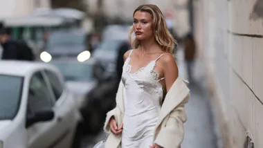 Chloe Lecareux seen wearing white silk laced long silk dress, beige long wool coat, white small shimmery handbag, silver big earrings and white high heels outside Georges Hobeika Show during the Haute Couture Spring/Summer 2024 as part of Paris Fashion Week on January 22, 2024 in Paris, France.