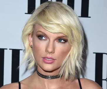 Short blonde-haired woman with blue eyes wearing a black choker, looking to the side at a formal event.