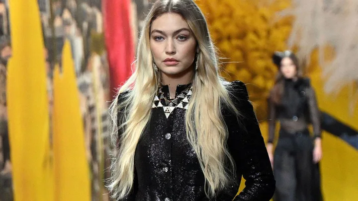 Model walks in Chanel Spring-Summer 2024 show, wearing black sequin outfit, bold geometric necklace, and long hair down.