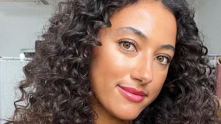 A woman with curly hair and bright eyes smiles softly in a close-up portrait.