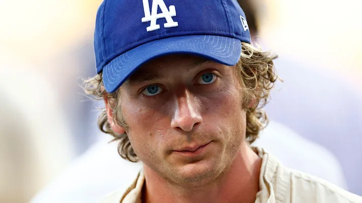 Man with blue eyes wearing a blue LA Dodgers cap and a light-colored shirt, looking serious.