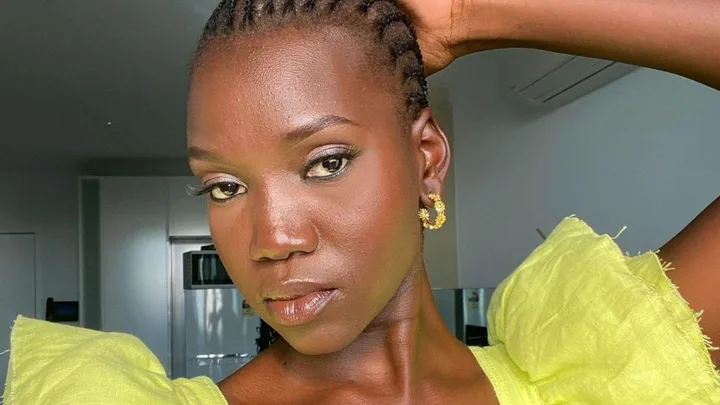 A person in a bright yellow top poses with one hand on their head, showcasing earrings and a neutral expression.