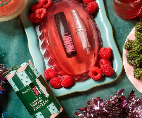 Benefit cosmetics displayed on a festive table with raspberries and greenery.