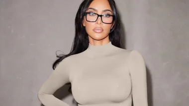 Woman in beige long-sleeved top and glasses against gray background.