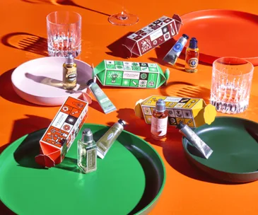 Colorful L'Occitane Christmas crackers and mini products on vibrant orange and green plates.