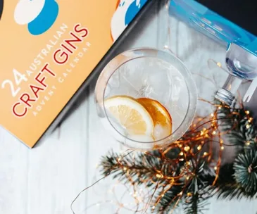 Australian craft gin advent calendar with a glass of gin and lemon slices, surrounded by fairy lights and pine branches.