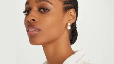 In this picture a beautiful model with locs swept back in an elegant bun wears the Mejuri drop pearl earings. These earings feature a small freshwater pearl with a larger "tear drop" pearl attached.