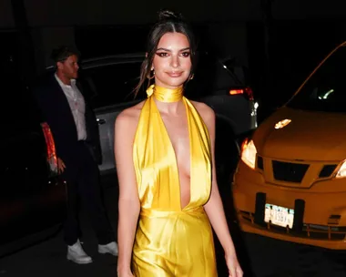 A woman in a yellow dress standing on a city street at night, with a taxi and a man in the background.