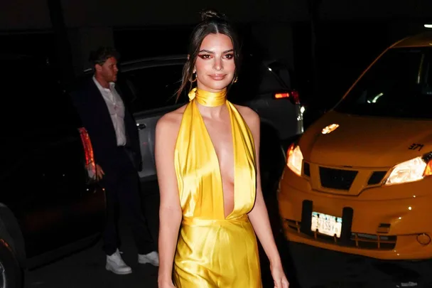 A woman in a yellow dress standing on a city street at night, with a taxi and a man in the background.