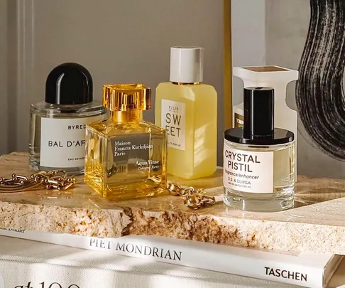 Perfume bottles on a stone slab with a chain and Piet Mondrian book in sunlight.