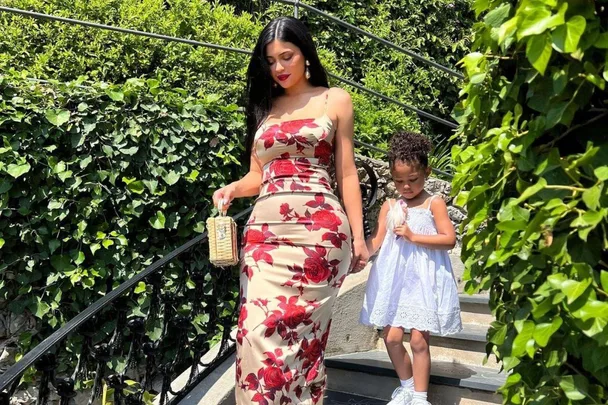 Woman in floral dress holding a child's hand while walking down stairs, surrounded by greenery.