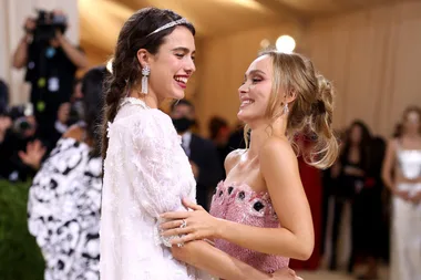 Two women smiling and embracing at a formal event, surrounded by photographers.