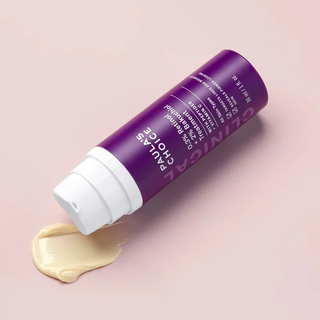 The Paula's Choice CLINICAL 0.3% Retinol + 2% Bakuchiol Treatment is a great retinol for beginners with plenty of conditioning ingredients. It comes in a cylindrical purple bottle with a white pump top. Pictured here with a swatch of the product which is a cream texture with a yellow tinge.