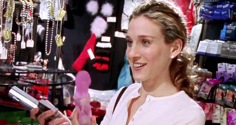 A woman smiling in a shop, holding a purple item among various accessories and merchandise.