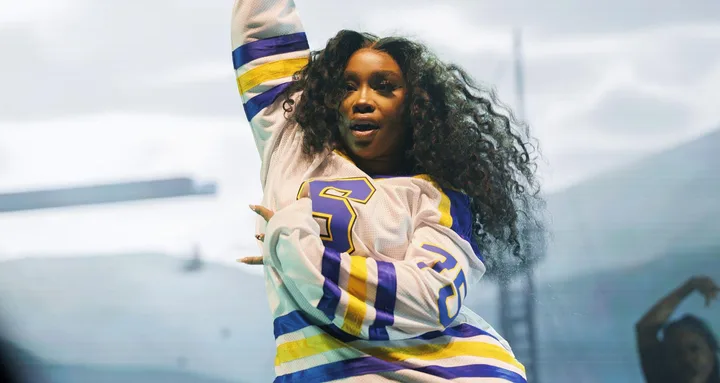 Singer performing energetically on stage, wearing a sports jersey with curly hair.