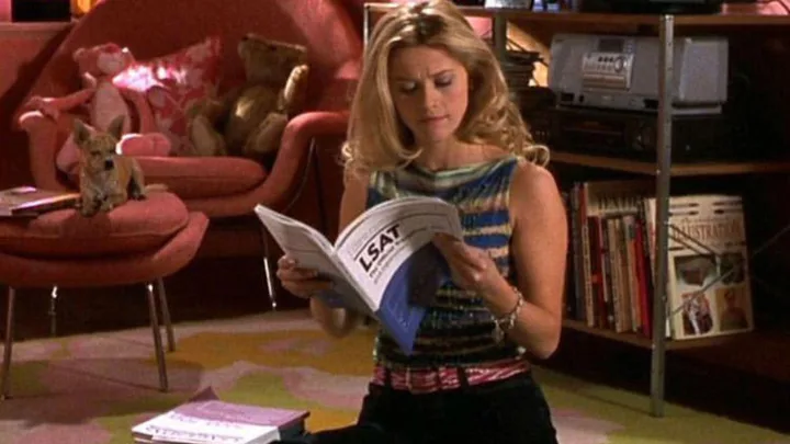 Woman reading LSAT book, sitting with a small dog on a cozy chair and plush toys in the background.