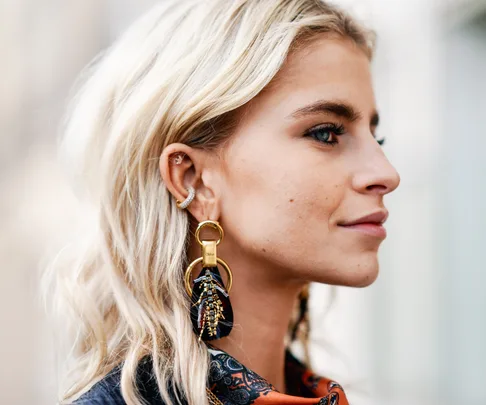 A woman with blonde hair wearing large, ornate hoop earrings and a colorful scarf, shown in profile.