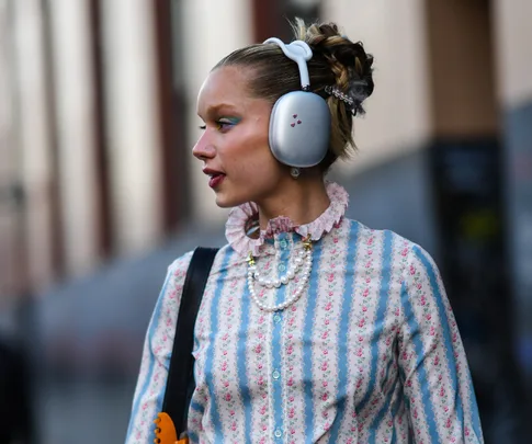 A woman wearing over-ear headphones and a vintage-style floral blouse with urban background.