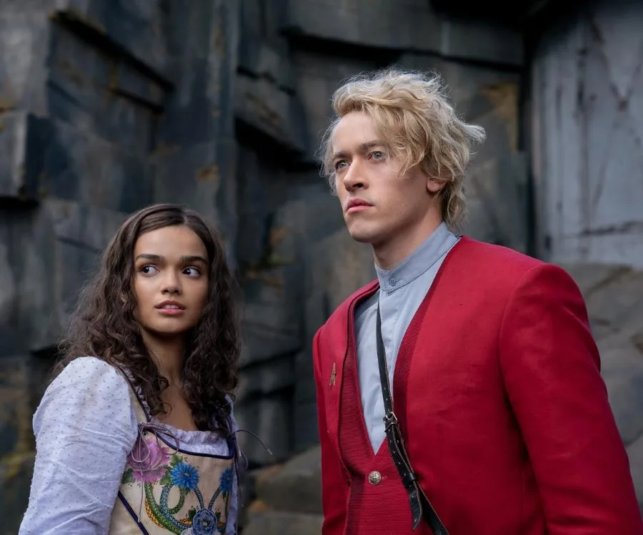 Two characters from "Hunger Games" prequel in a tense scene, wearing detailed costumes, against a rocky backdrop.