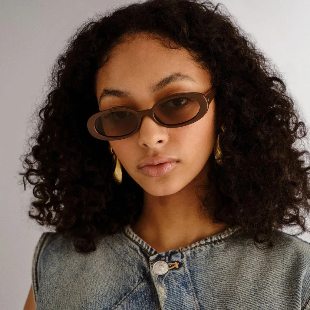 Model wearing oval Outta Love frames in "cocoa" from Le Specs