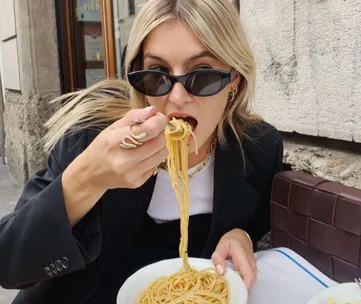 Person wearing sunglasses eating spaghetti at an outdoor cafe.