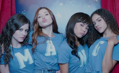 Four young women wearing blue shirts with letters "MANG" pose together against a starry backdrop.