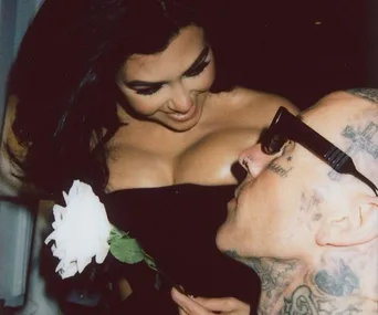 Couple sharing a tender moment; woman holds a white rose while looking down at a tattooed man gazing up at her.