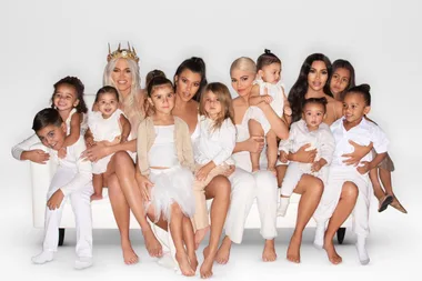 A large family group sitting on a white couch, wearing coordinated white outfits, smiling at the camera.