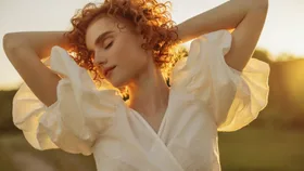 A redhead girl smiling in the sunlight wearing a puff sleeved white dress.