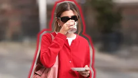 Girl in a red cardigan drinks from a coffee cup.